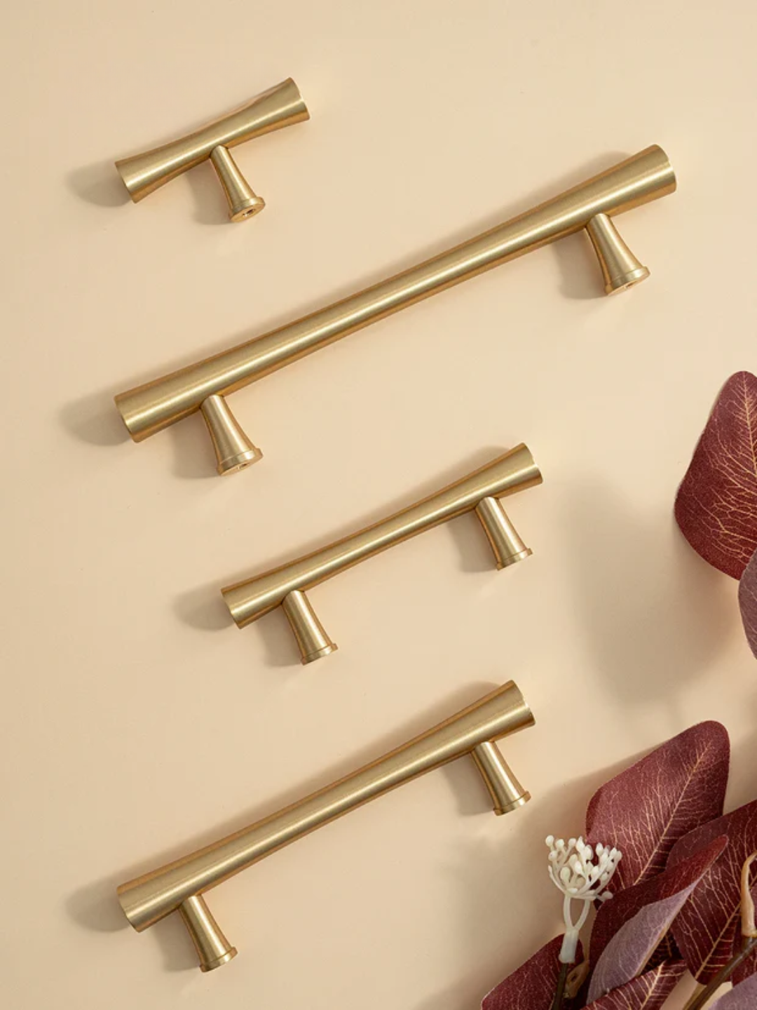 Set of gold cabinet handles on a beige background with leaves.