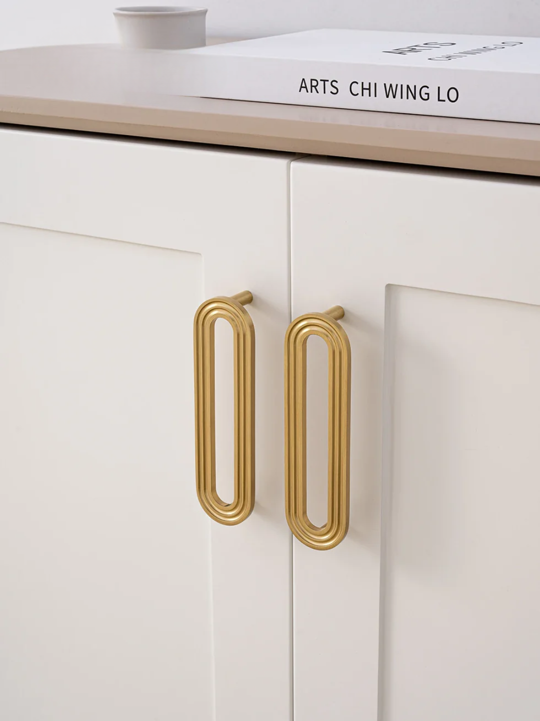 Close-up of a white cabinet with gold handles and a book on top.