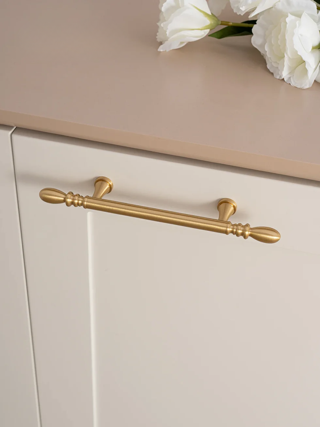 Gold cabinet handle on a light-colored cabinet with white flowers on top