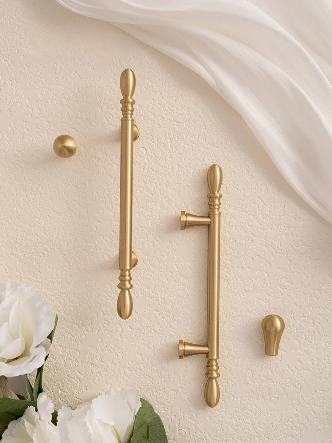 Gold cabinet handles on a beige wall with white flowers in the foreground