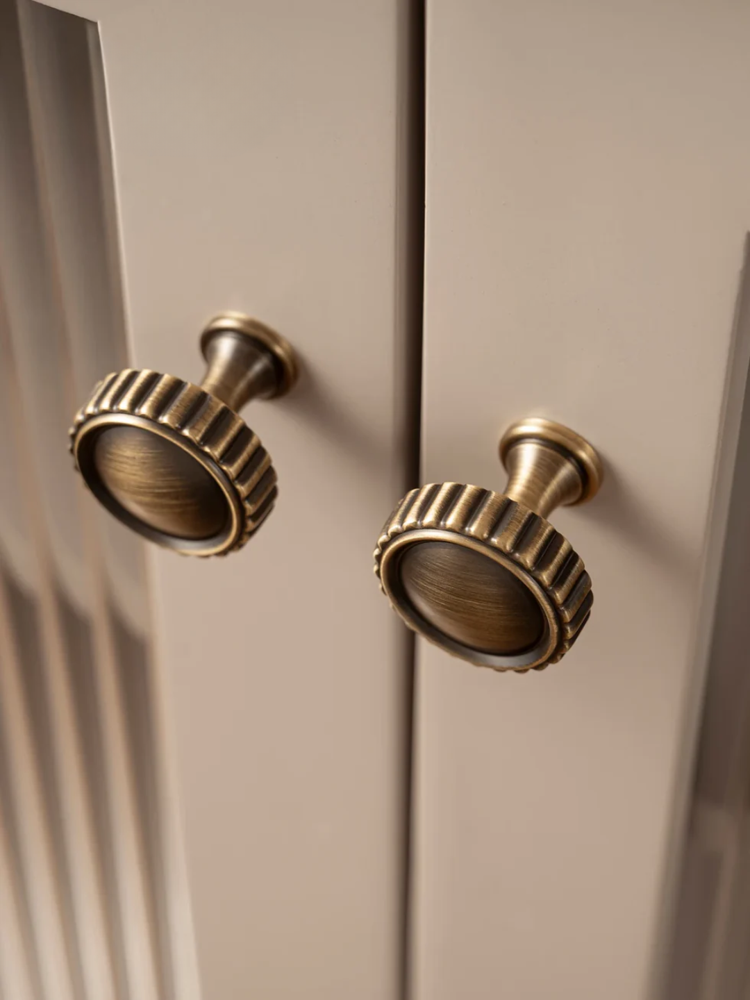 Close-up of two brass cabinet knobs on a beige cabinet.