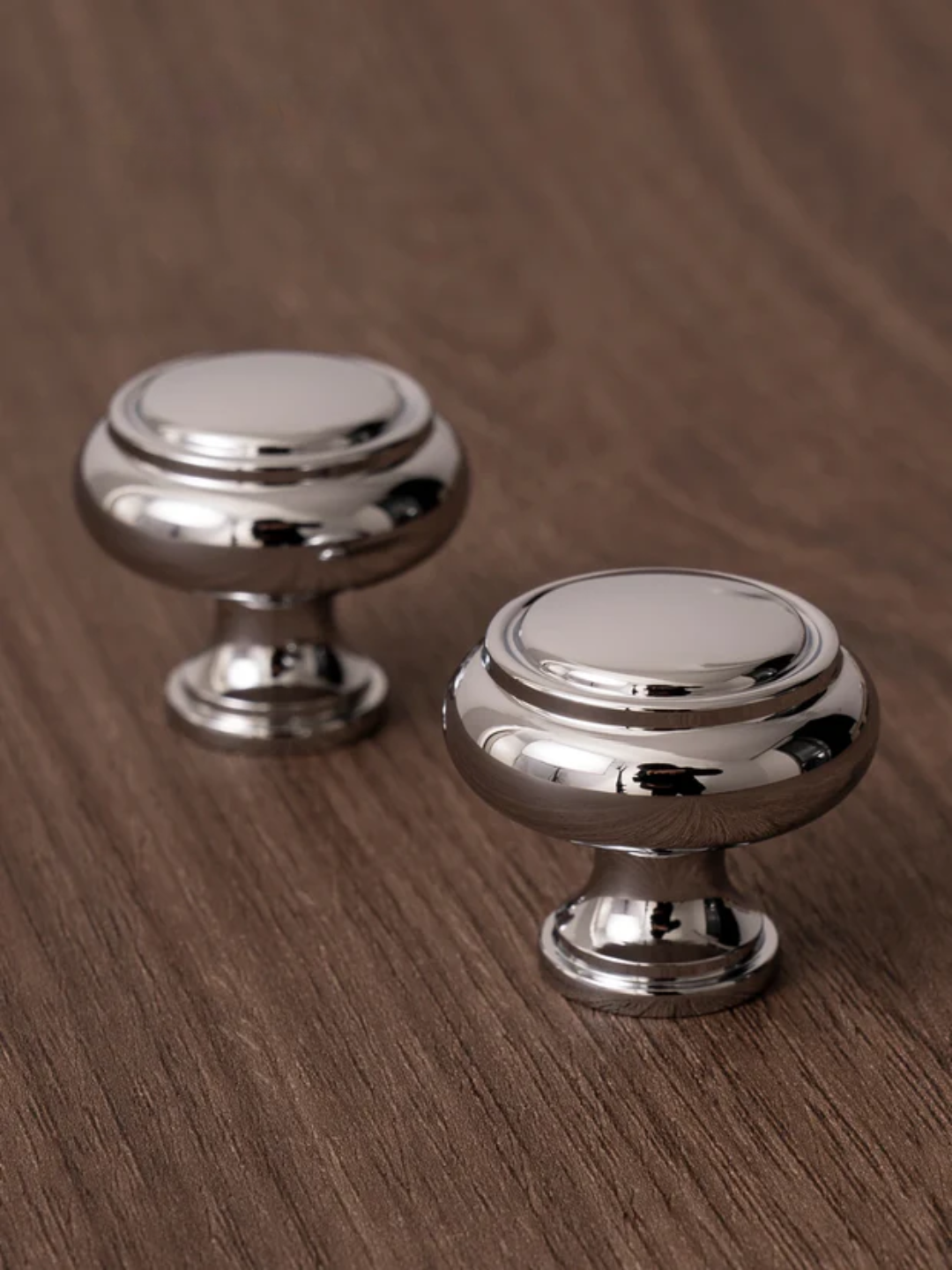 Two silver cabinet knobs on a wooden surface