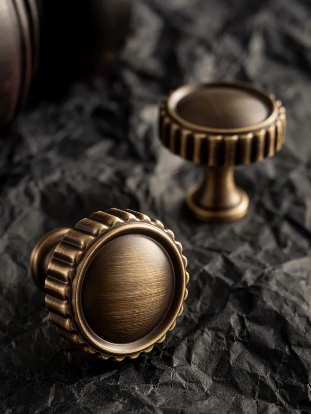 Two bronze cabinet knobs on a textured black surface