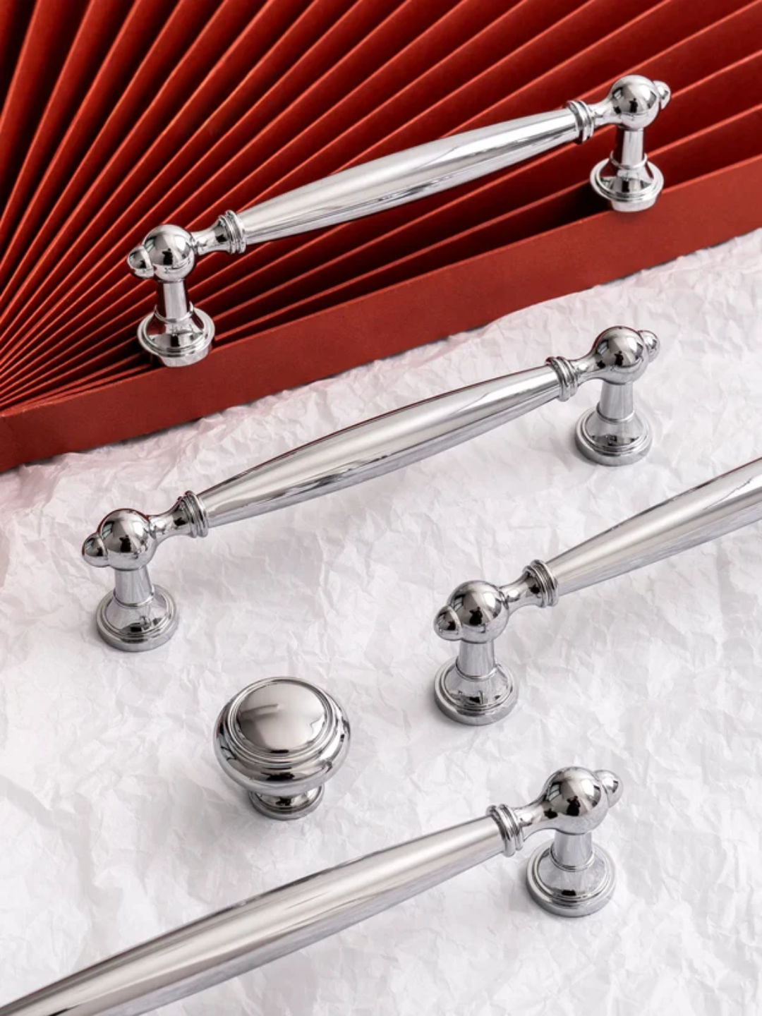 Set of silver cabinet handles on a white surface with a red textured background