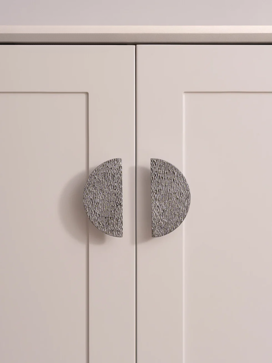 Close-up of a light gray cabinet with round textured knobs on a neutral background