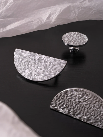 Silver half-circle earrings on a black surface with crumpled white paper in the background.