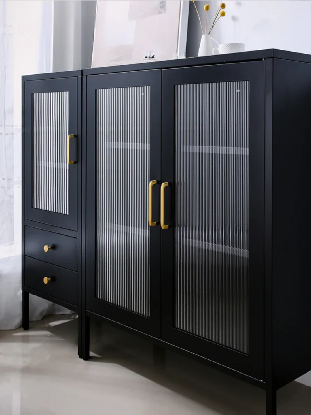 Black cabinet with glass doors and gold handles in a room setting.