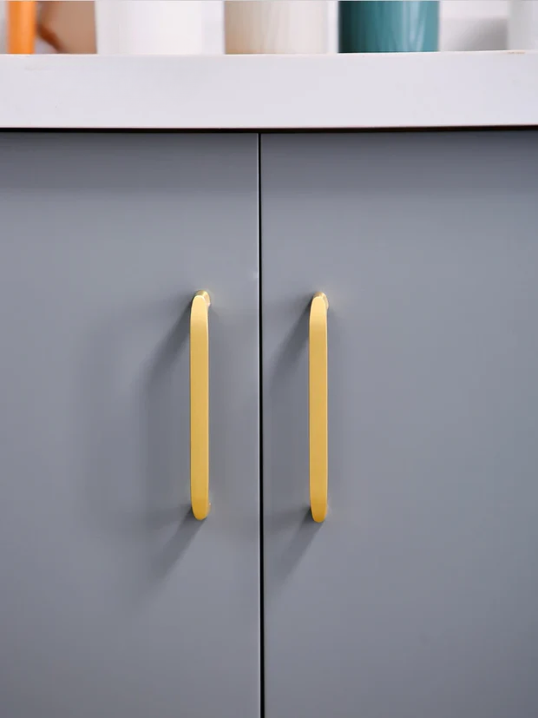 Gray cabinet with gold handles on a white countertop.