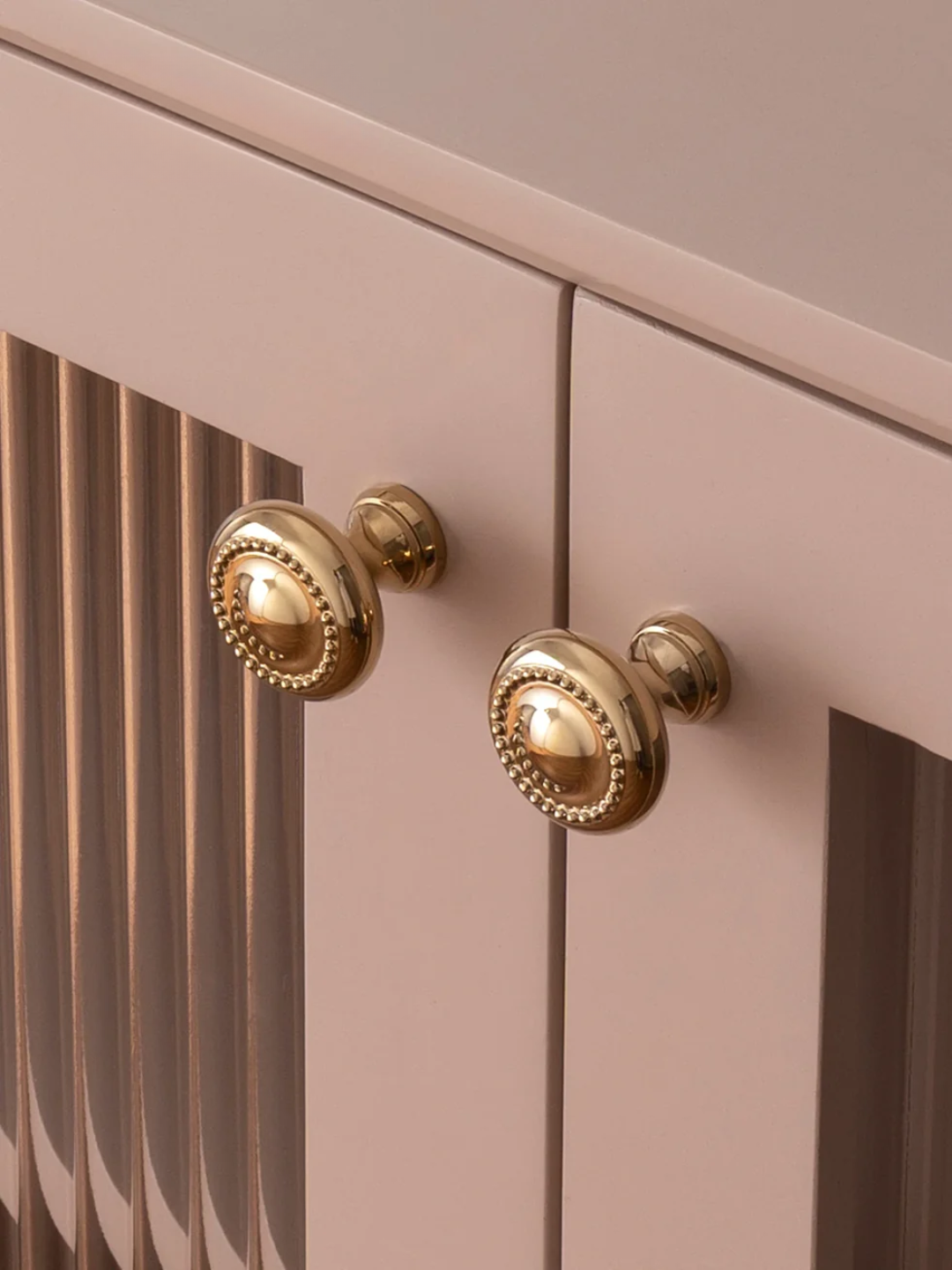 Close-up of a pink cabinet with gold knobs
