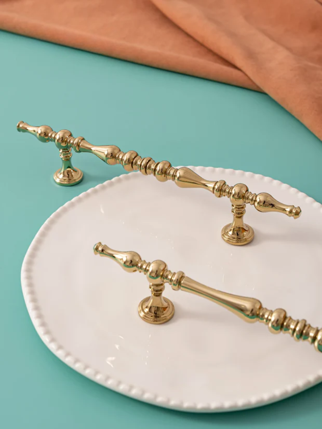 Gold decorative handles on a white plate with a teal background