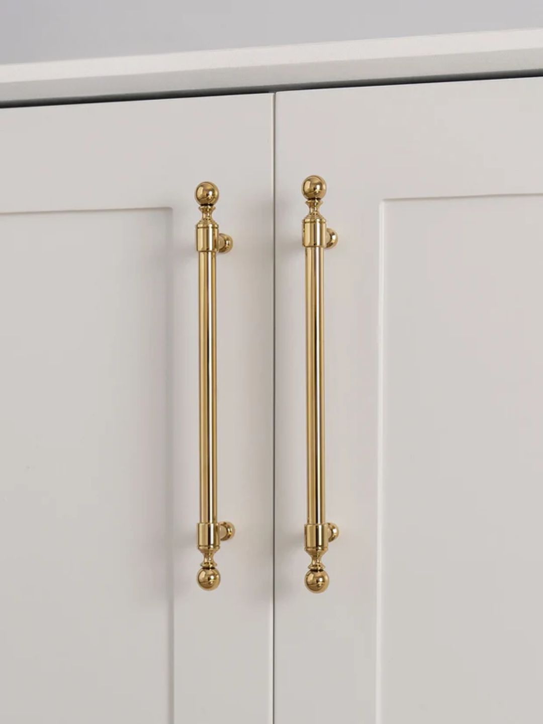 Close-up of a pair of white cabinet doors with gold handles on a light gray background.