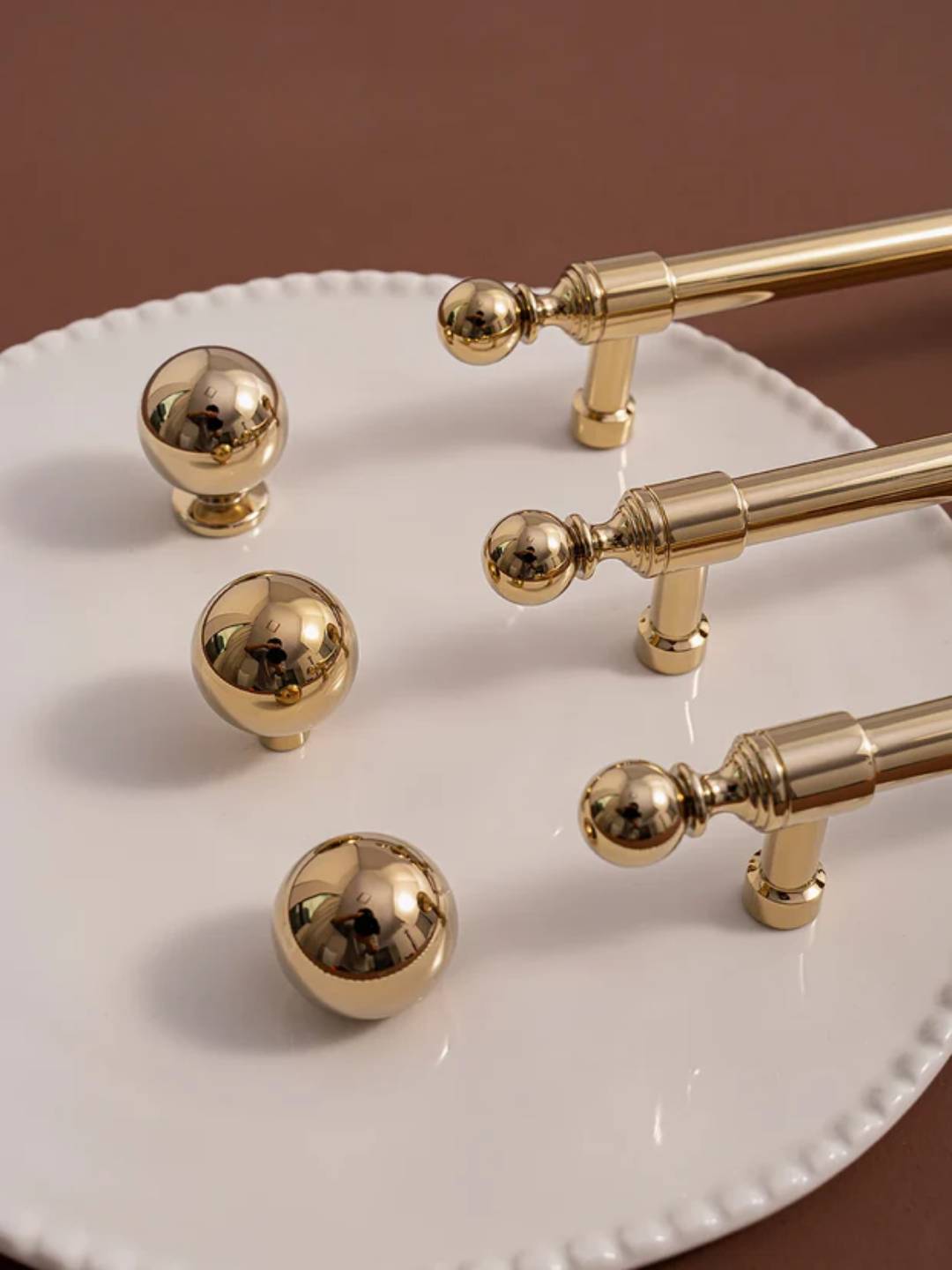 Gold handles and knobs on a white plate with a brown background