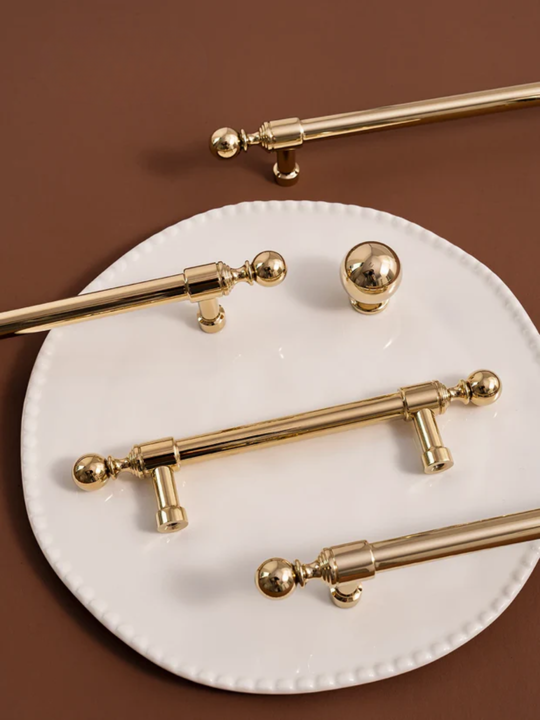 Gold cabinet handles on a white plate with a brown background