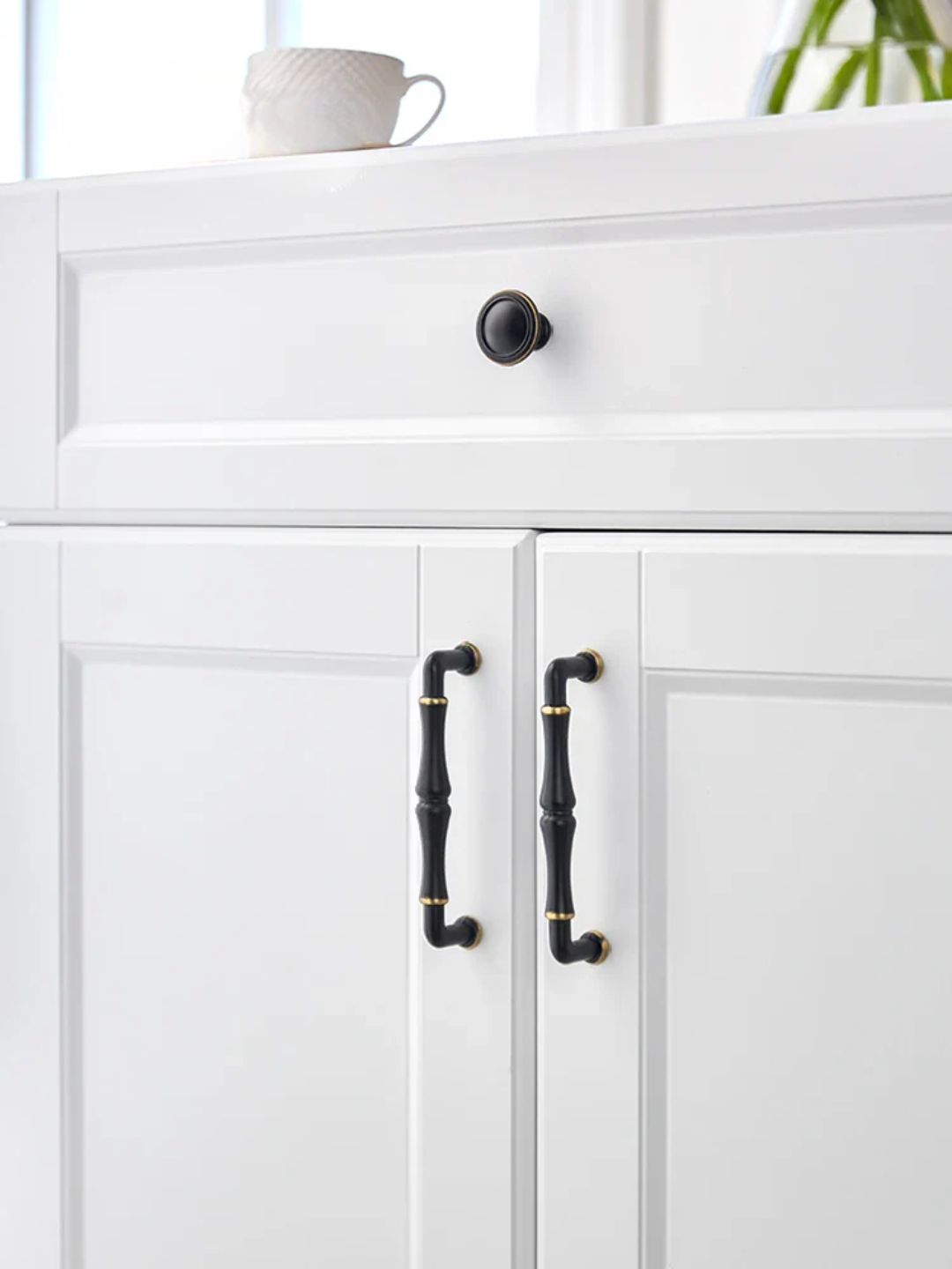 White cabinet with black handles and a small plant in the background