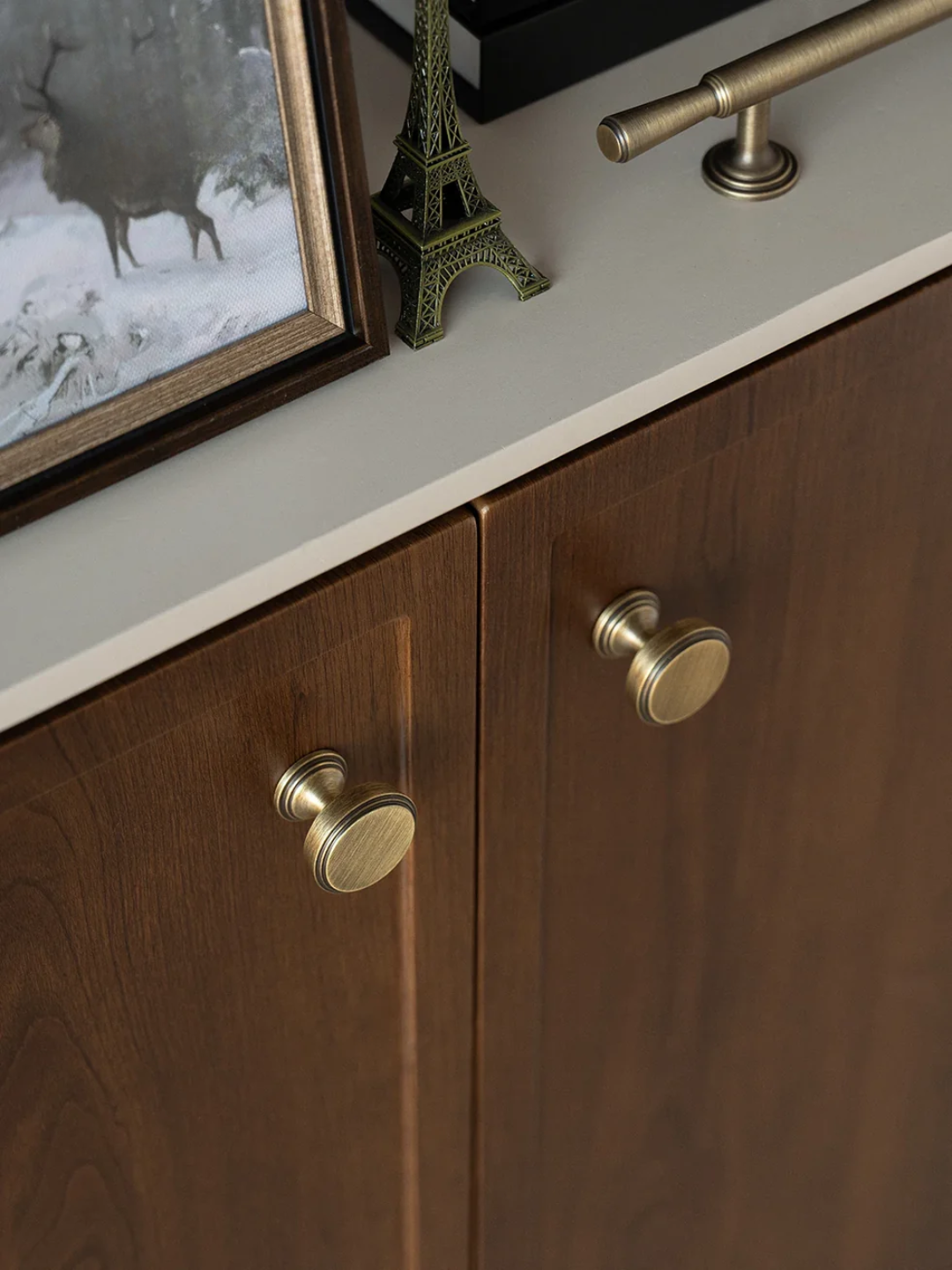 Wooden cabinet with brass knobs and a framed picture of a deer on a snowy background.