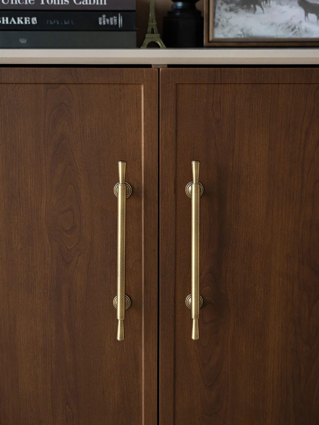 Wooden cabinet with gold handles on a shelf with books and decor items.