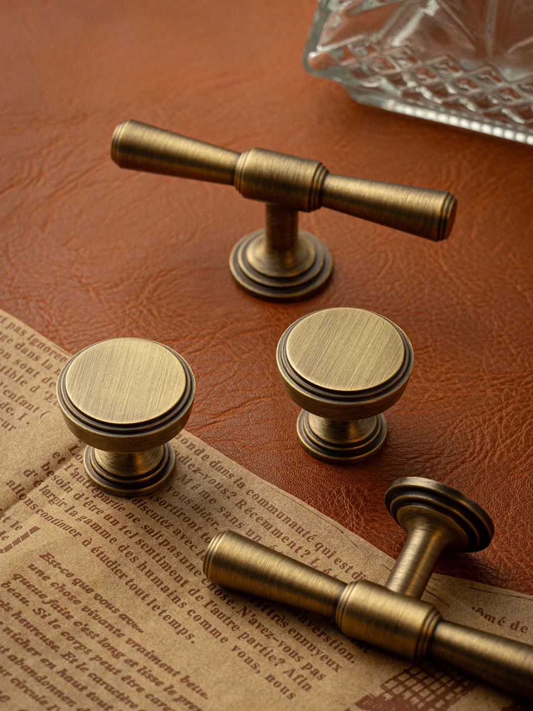 Set of brass cabinet knobs on a textured surface with a glass dish in the background