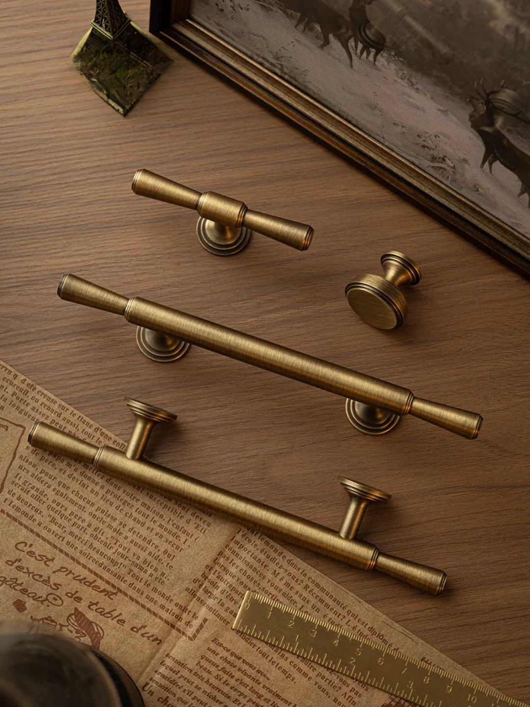 Set of brass cabinet handles on a wooden surface with a map and decorative frame in the background.