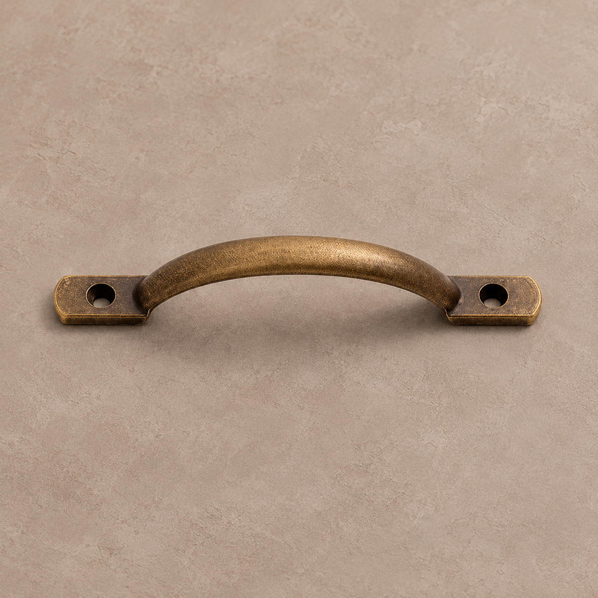 Antique brass cabinet pull on a warm taupe studio background