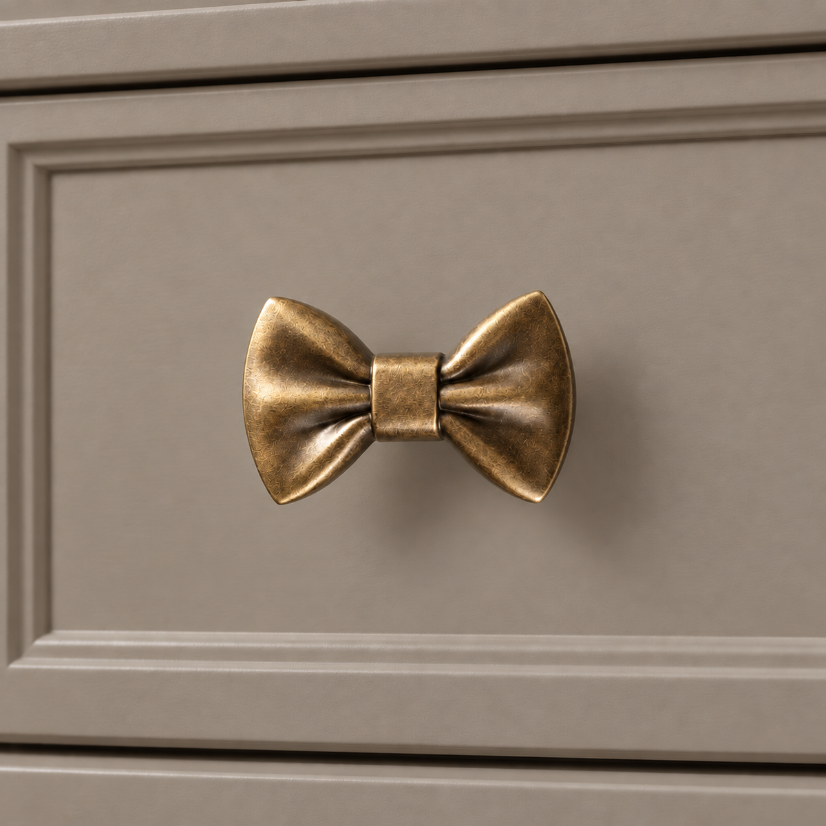 Antique brass bow-tie knob mounted on a taupe cabinet