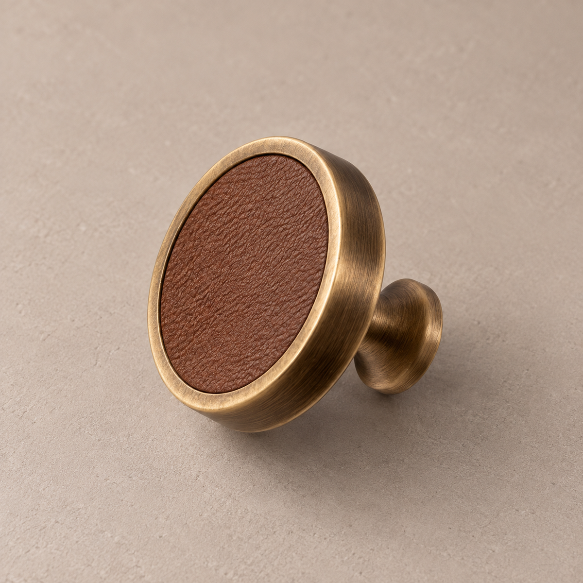 Antique brass cabinet knob with brown cowhide leather inlay on taupe studio background