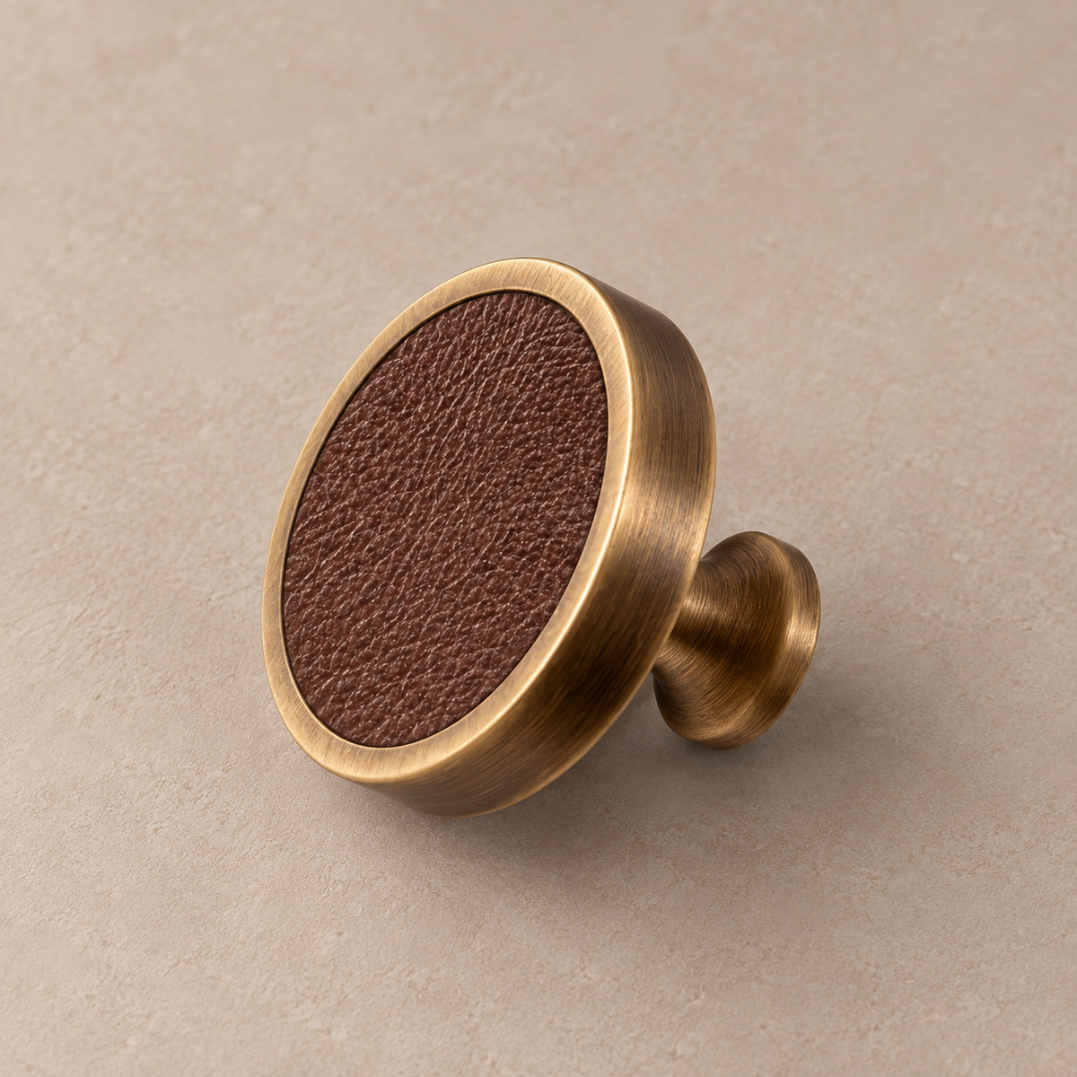 Antique brass cabinet knob with coffee cowhide leather inlay on taupe studio background