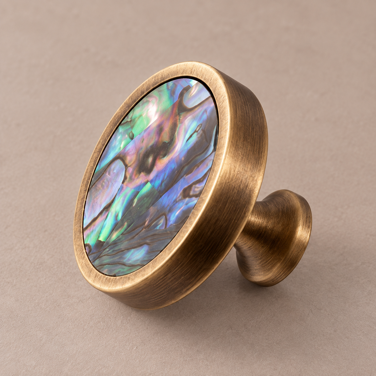 Antique brass round cabinet knob with green abalone shell inlay on taupe studio background