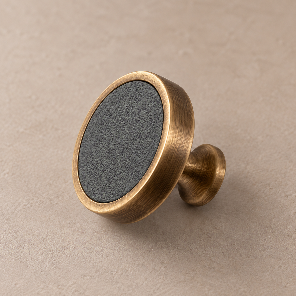 Antique brass cabinet knob with grey cowhide leather inlay on taupe studio background