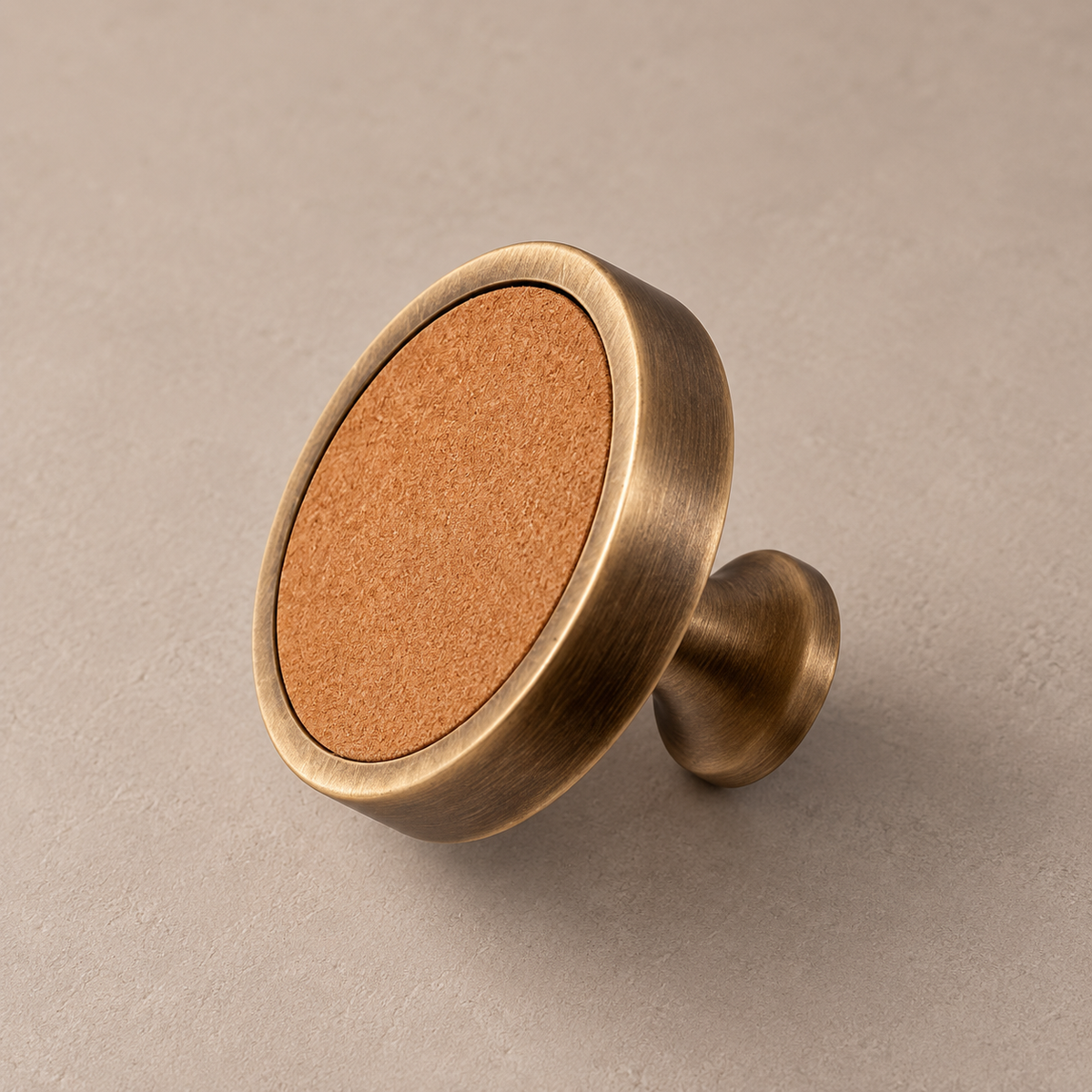 Antique brass cabinet knob with khaki cowhide leather inlay on taupe studio background