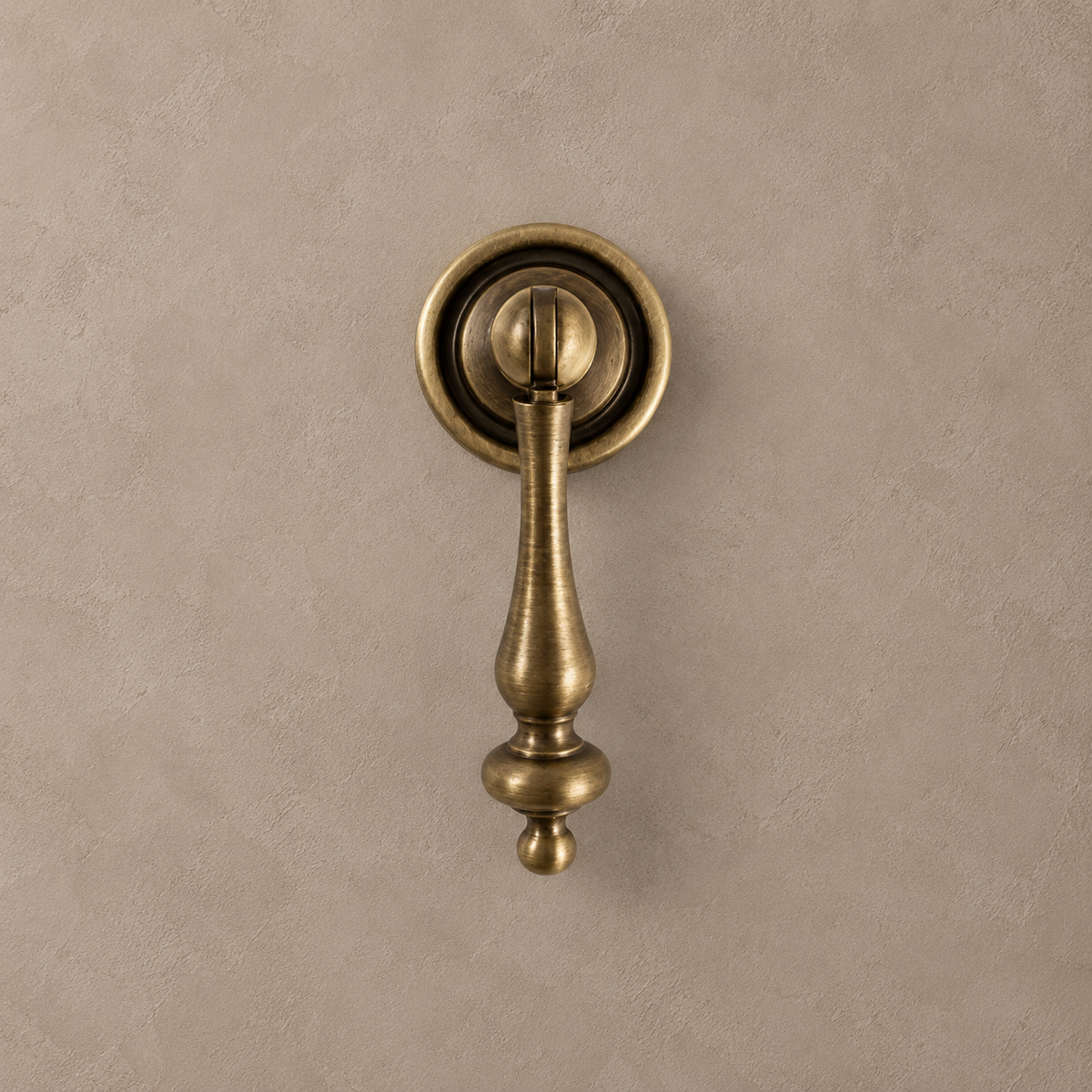 Antique brass small pendant cabinet pull with round backplate on a warm taupe background
