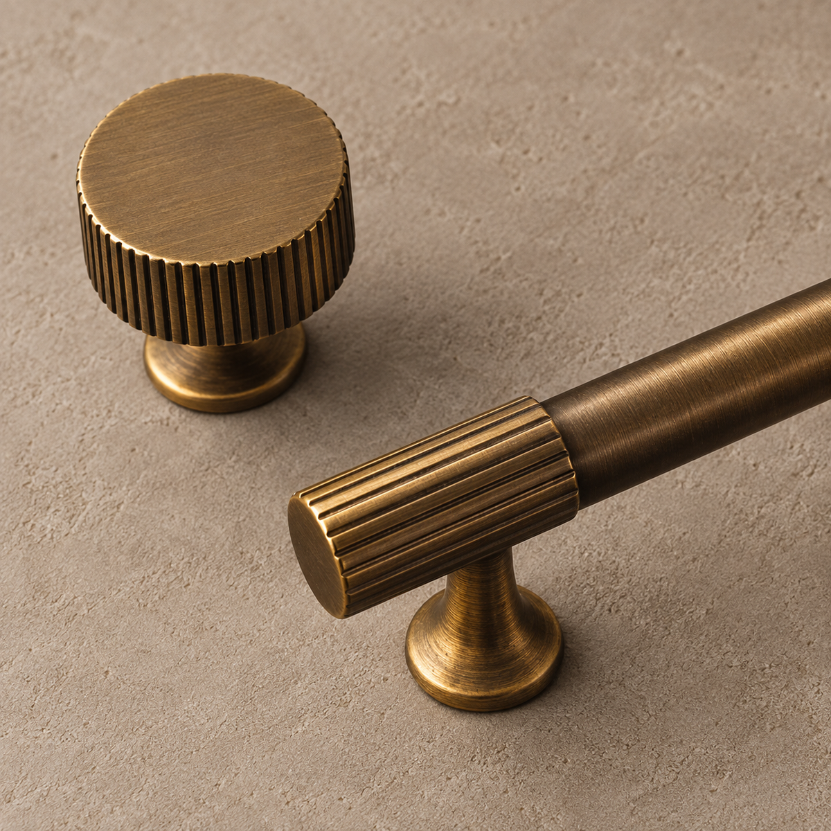 Close-up of antique brass ribbed knob and fluted cabinet pull end on a taupe studio background
