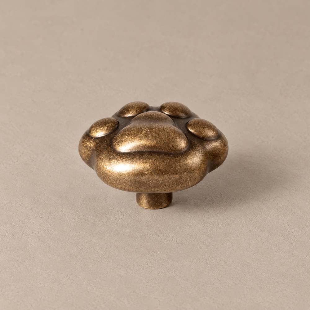 antique brass sculpted cat paw cabinet knob with four rounded toes and central paw pad, short smooth cylindrical mounting post on taupe studio surface
