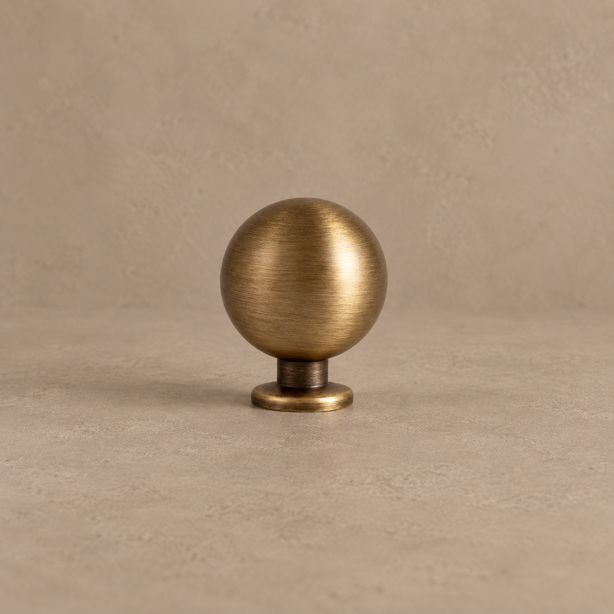 Antique brushed brass round cabinet knob on a warm taupe studio background