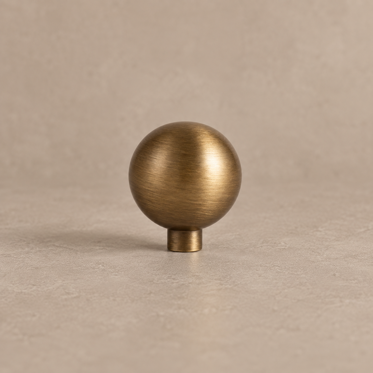 Antique brushed brass round cabinet knob on a warm taupe studio background
