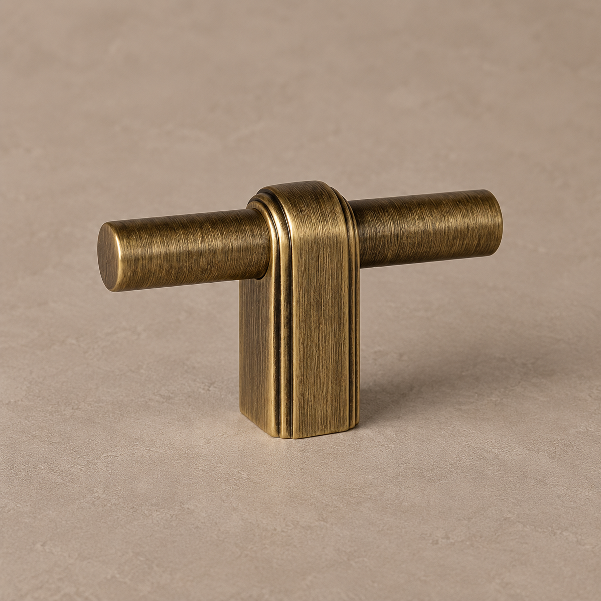 antique brass T knob, cylindrical horizontal bar through a rounded rectangular central post with parallel edge grooves on warm taupe surface