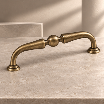 Arched Bail Cabinet Pull & Knob — Antique Brass on a neutral stone studio background