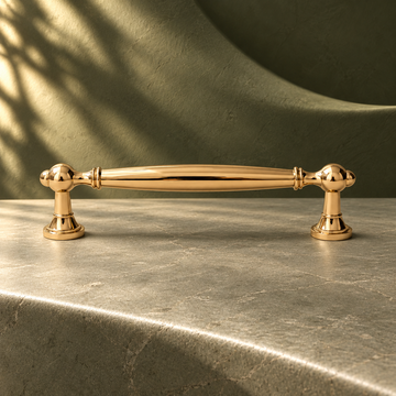 Polished gold spindle cabinet pull with round pedestal feet on a deep olive studio background