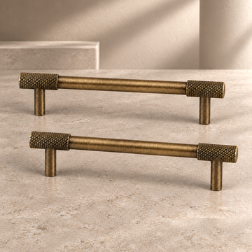 Solid Brass Cross Knurled Cabinet Pulls & Knobs — Antique Brass Finish on a neutral stone studio background