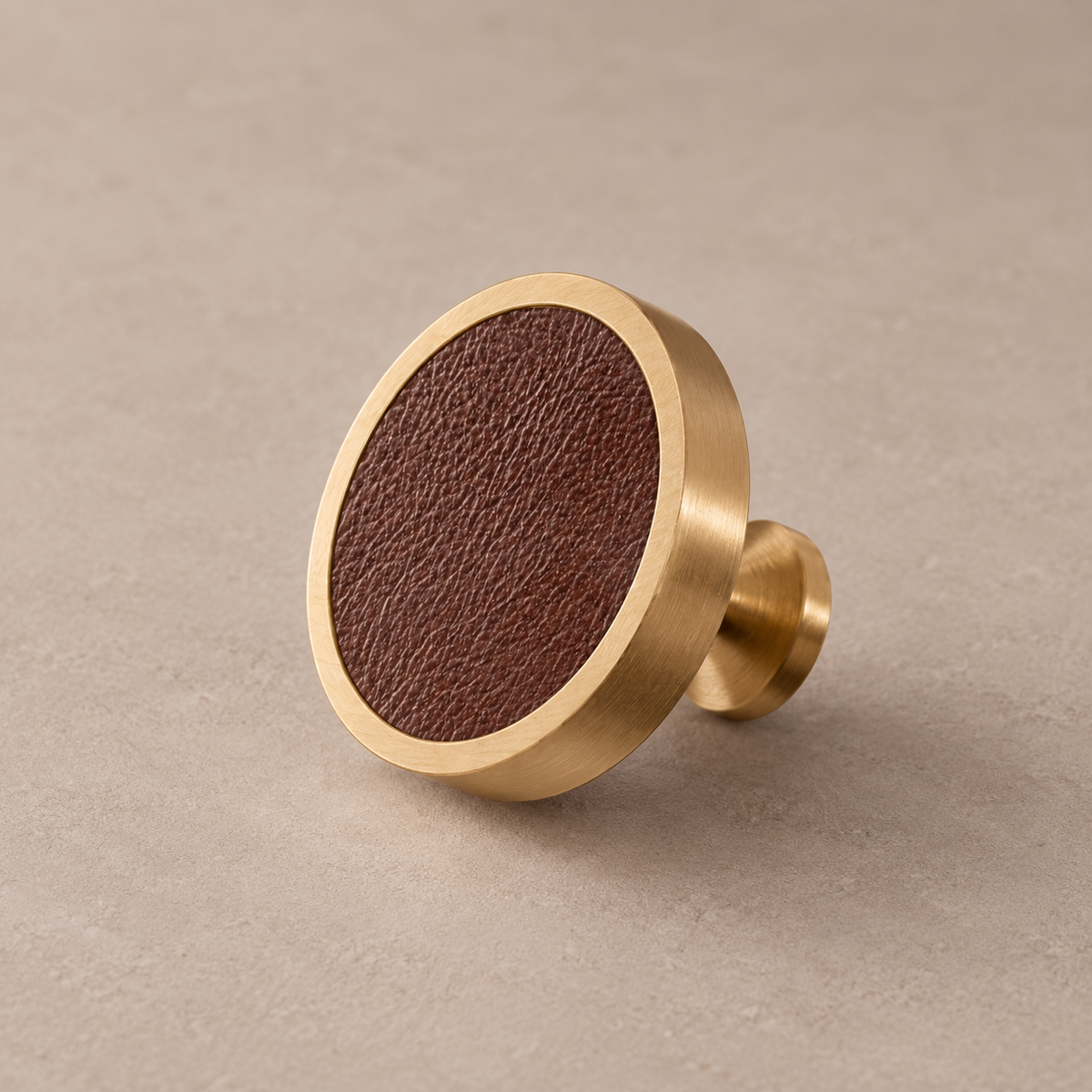Brushed brass cabinet knob with coffee brown cowhide leather inlay on taupe studio background