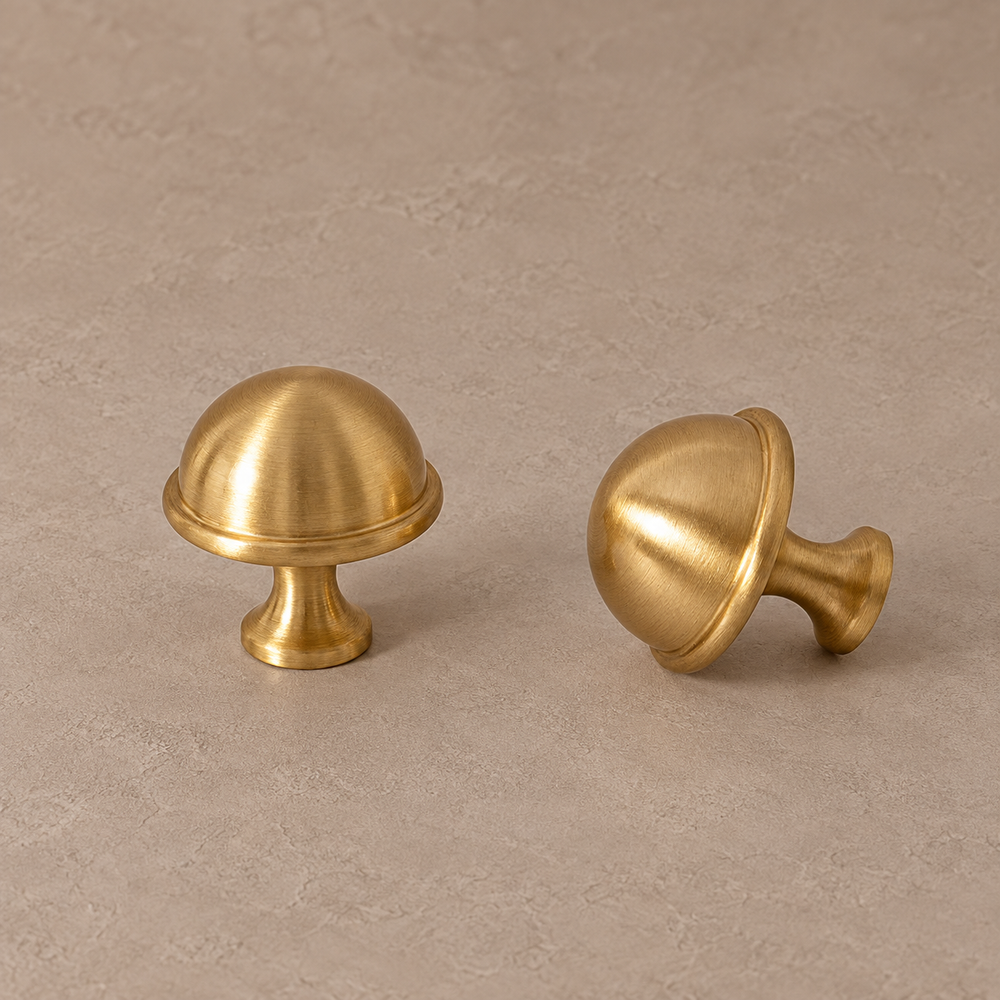 brushed brass dome knob with narrow raised rim, flared neck and circular base on a warm taupe studio background