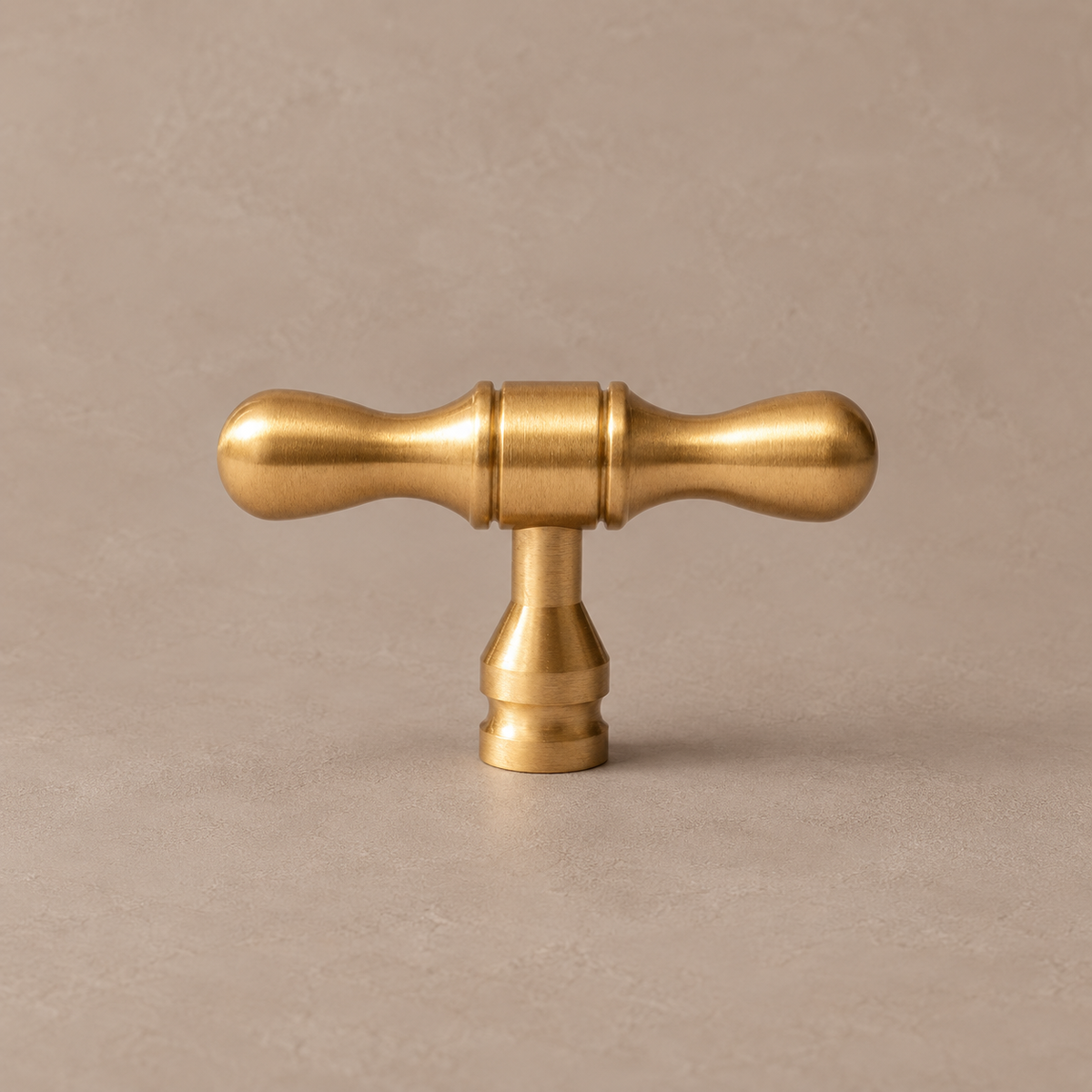 Brushed brass drop-shaped T knob on warm taupe studio background