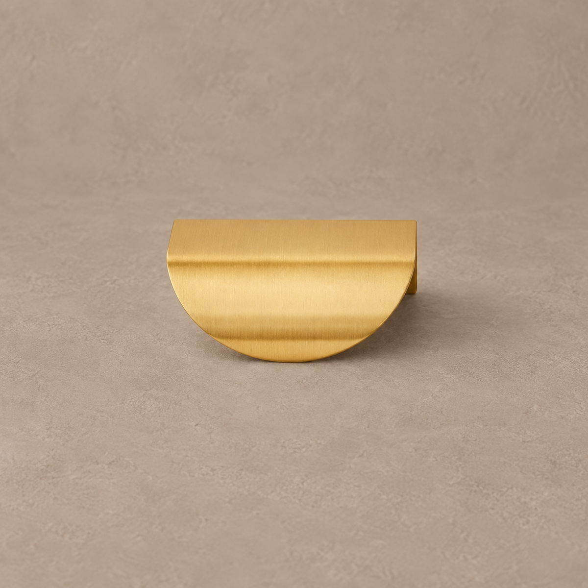 Brushed brass cabinet finger pull on taupe studio background