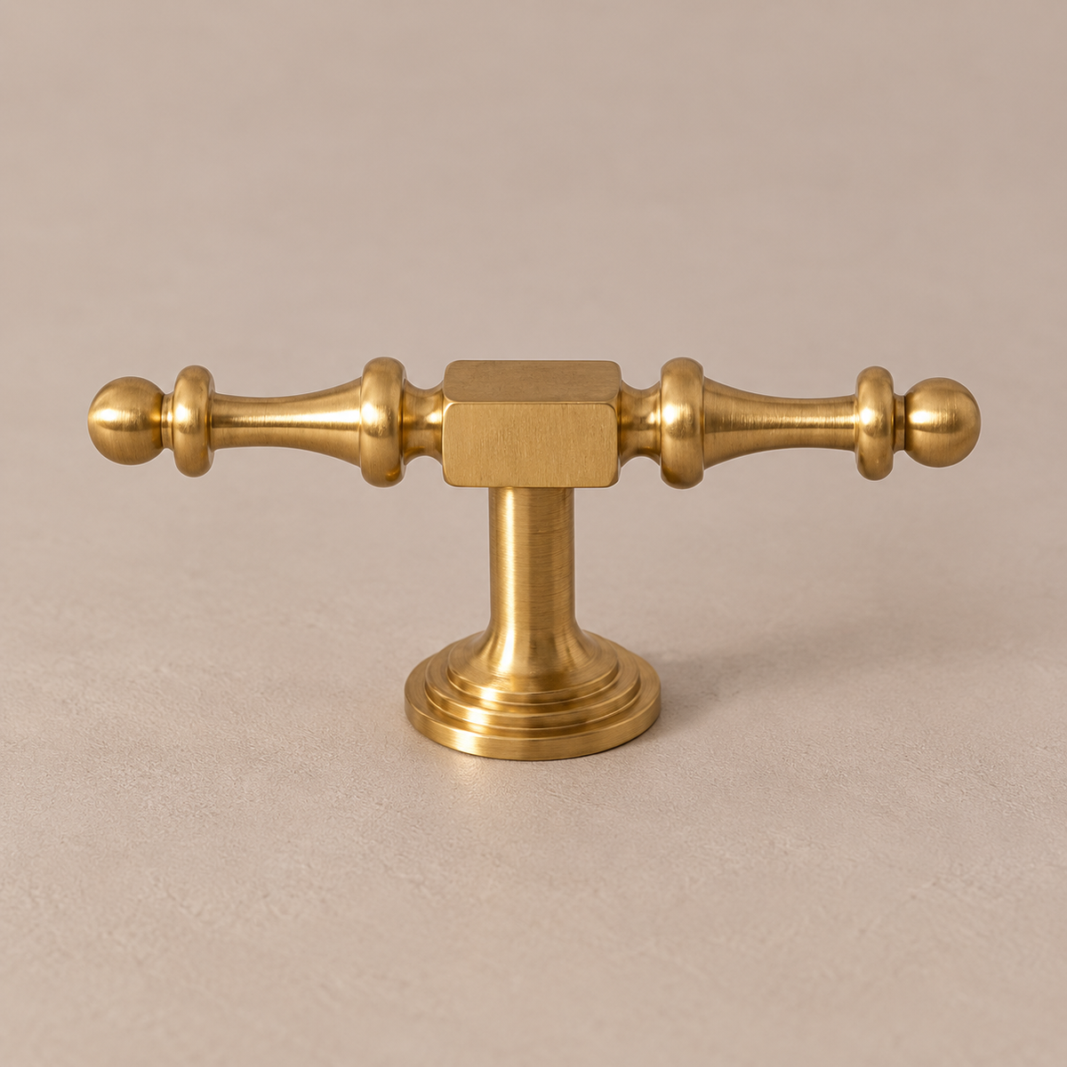 brushed brass finial t knob on a warm taupe studio surface