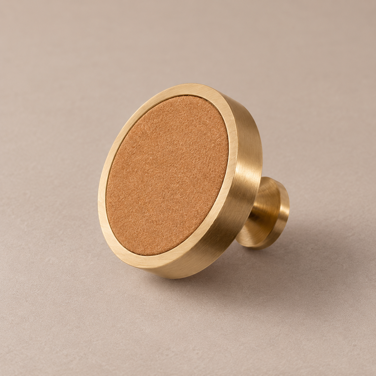 Brushed brass cabinet knob with khaki cowhide leather inlay on taupe studio background