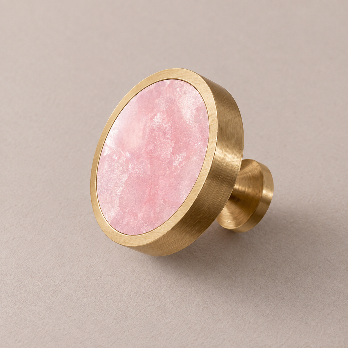 Brushed brass cabinet knob with pink shell inlay on taupe studio background