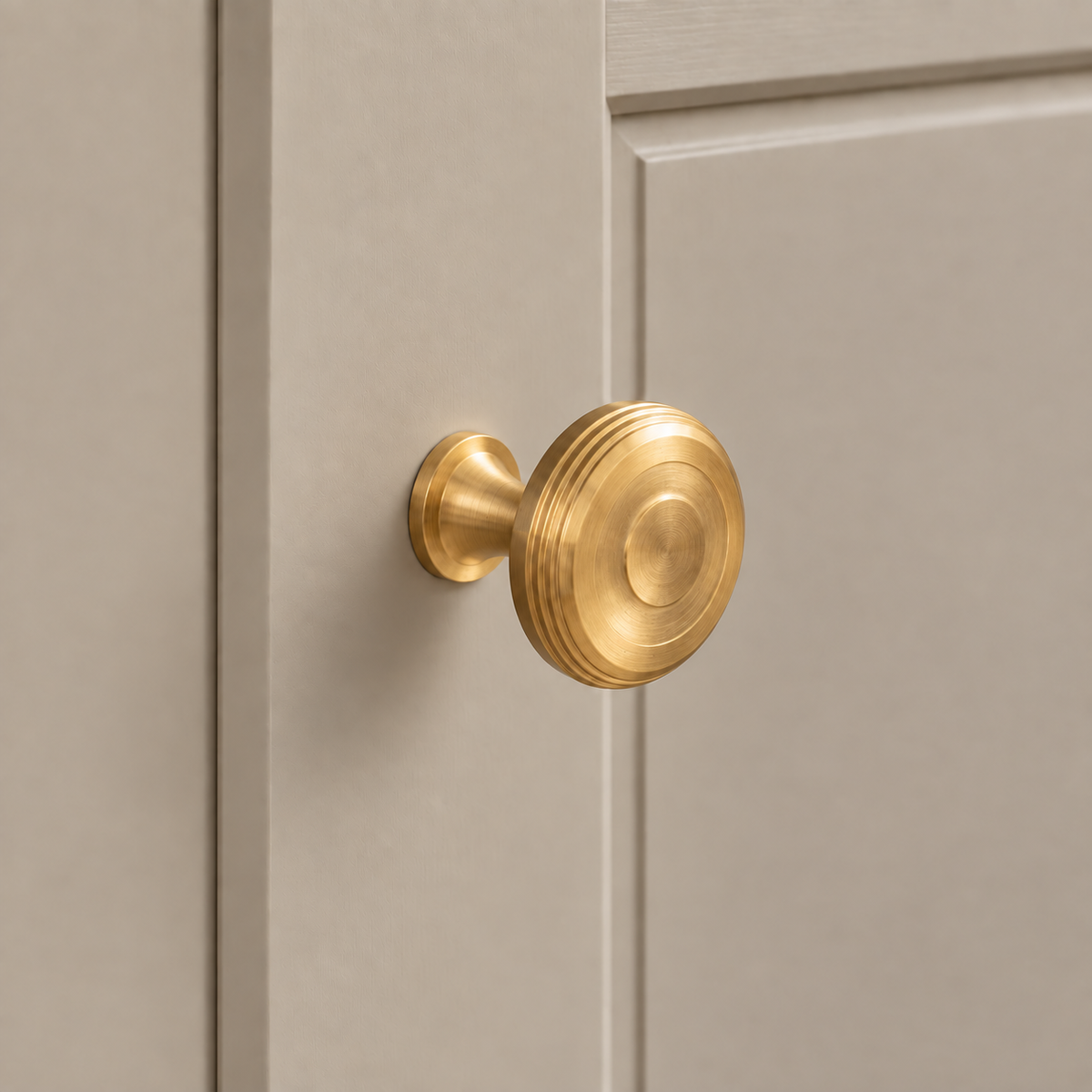 Round brushed brass cabinet knob with concentric face and grooved rim mounted on taupe cabinetry