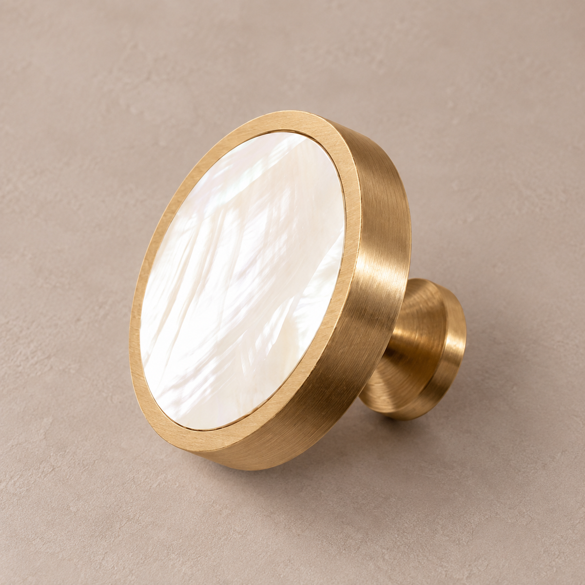 Brushed brass round cabinet knob with white mother-of-pearl shell inlay on taupe studio background