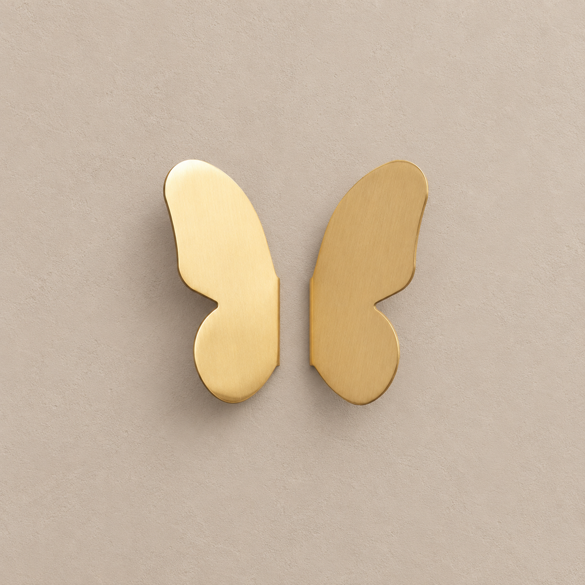 pair of brushed brass butterfly-wing cabinet knobs, two separate mirrored wings on a warm taupe background