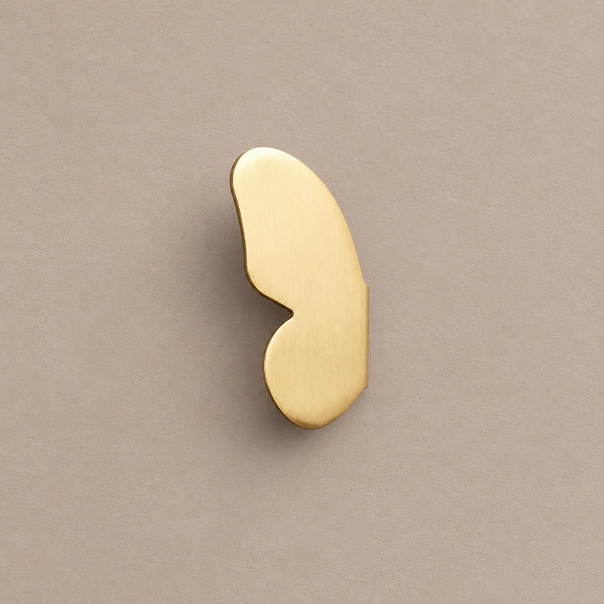 one brushed brass left butterfly-wing cabinet knob on a warm taupe background
