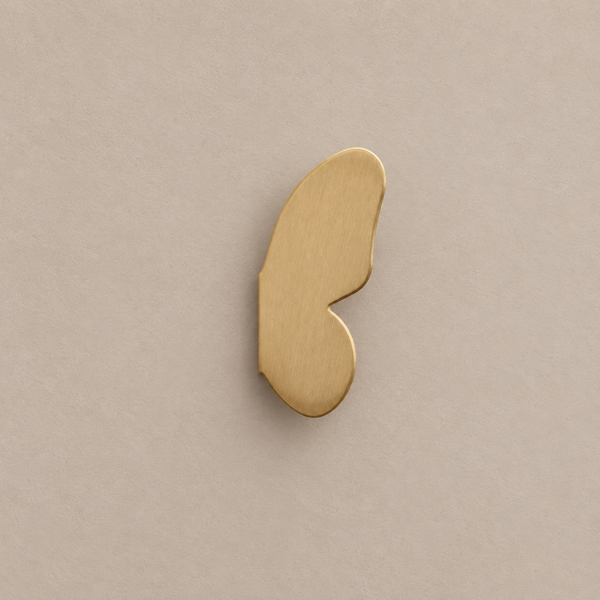 one brushed brass right butterfly-wing cabinet knob on a warm taupe background